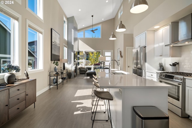 kitchen featuring white cabinetry, high vaulted ceiling, pendant lighting, wall chimney exhaust hood, and stainless steel appliances