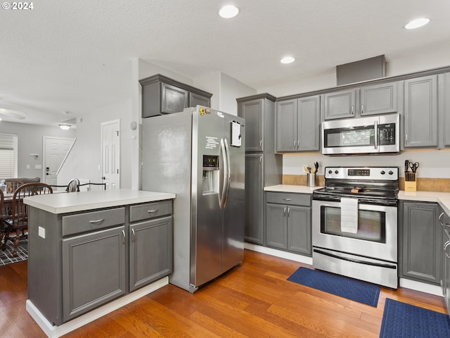 kitchen with dark wood-type flooring, appliances with stainless steel finishes, gray cabinetry, and a kitchen island