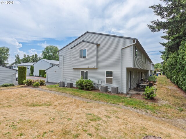 rear view of property with central air condition unit, a lawn, and a patio