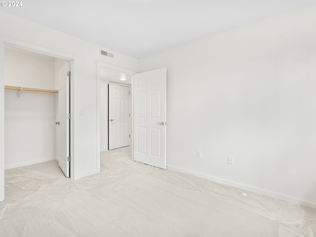 unfurnished bedroom featuring a walk in closet, light colored carpet, and a closet