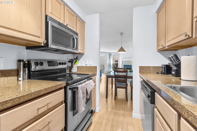 kitchen with light brown cabinets, sink, hanging light fixtures, light hardwood / wood-style flooring, and stainless steel appliances