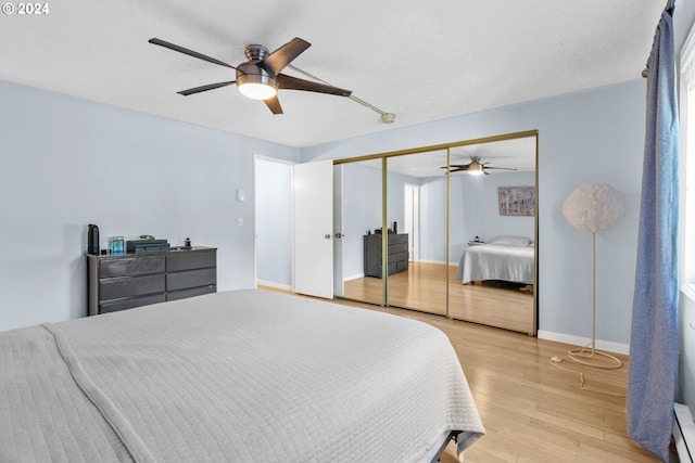 bedroom with ceiling fan, a baseboard heating unit, light wood-type flooring, and a closet