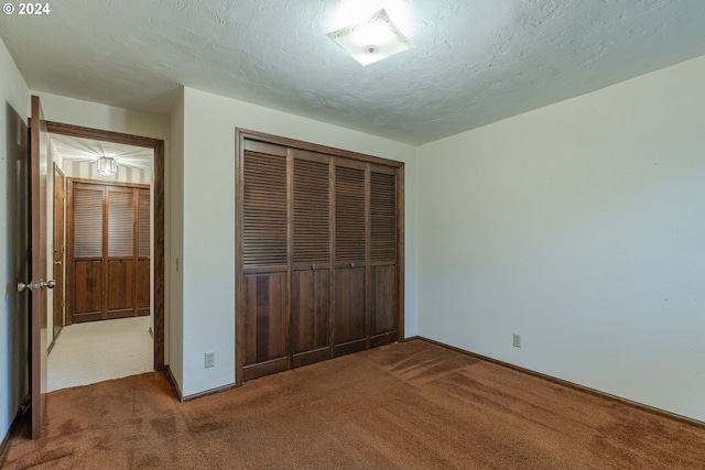 unfurnished bedroom featuring a textured ceiling, a closet, and dark colored carpet