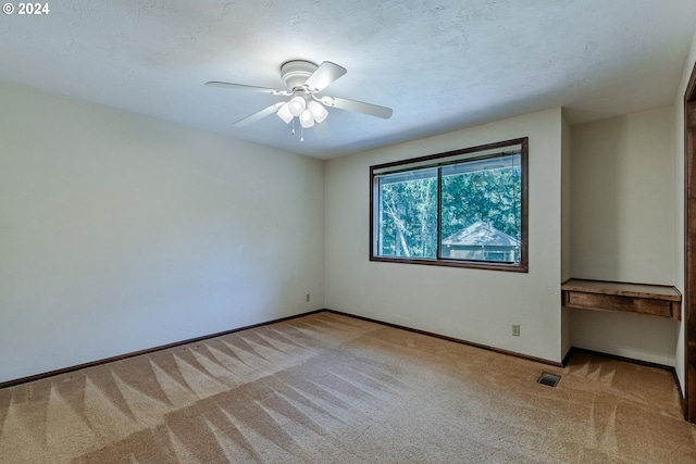 empty room featuring ceiling fan, light colored carpet, and a textured ceiling