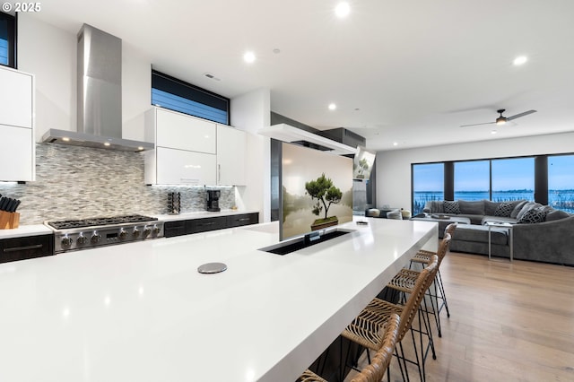 kitchen featuring wall chimney range hood, a kitchen bar, light countertops, stove, and white cabinetry