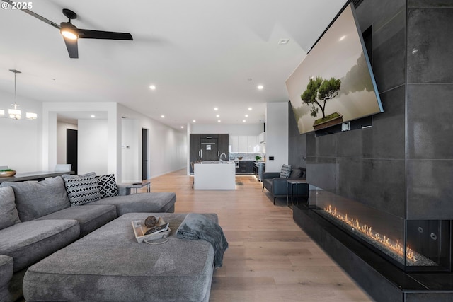 living room featuring a ceiling fan, recessed lighting, light wood finished floors, and a large fireplace