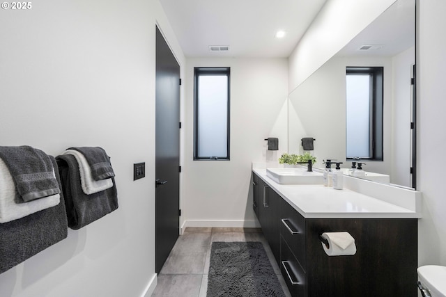 bathroom with visible vents, toilet, a sink, double vanity, and baseboards