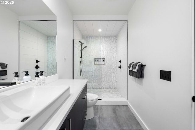 bathroom with baseboards, tiled shower, toilet, and vanity