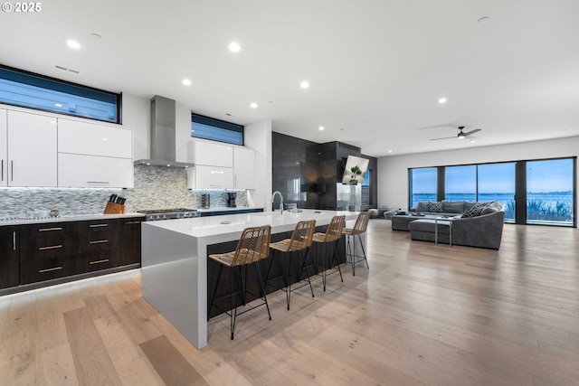 kitchen featuring wall chimney range hood, a large island, white cabinetry, a kitchen breakfast bar, and modern cabinets