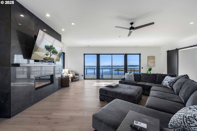 living area with a large fireplace, a barn door, recessed lighting, light wood-style flooring, and a ceiling fan