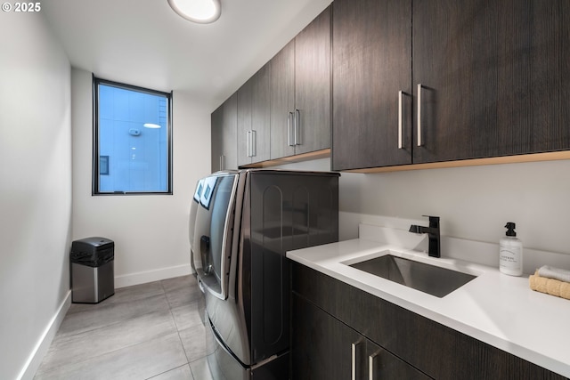 laundry area featuring baseboards, light tile patterned flooring, cabinet space, a sink, and washer and clothes dryer