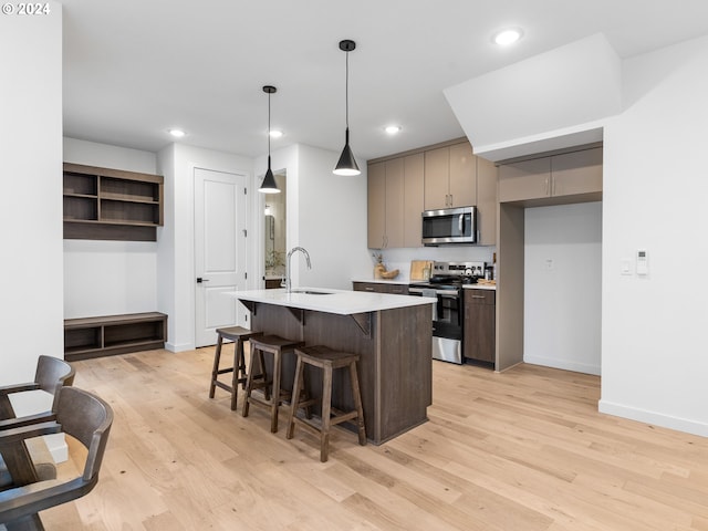 kitchen with sink, hanging light fixtures, stainless steel appliances, light hardwood / wood-style flooring, and an island with sink