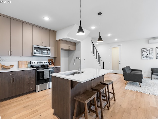 kitchen featuring stainless steel appliances, sink, decorative light fixtures, light hardwood / wood-style flooring, and a center island with sink