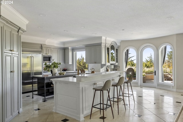 kitchen with a breakfast bar, built in appliances, gray cabinets, a textured ceiling, and a center island