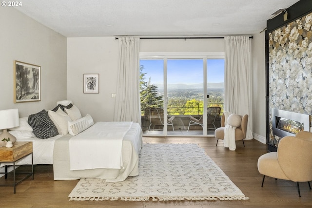 bedroom with a large fireplace, dark wood-type flooring, a mountain view, and access to exterior