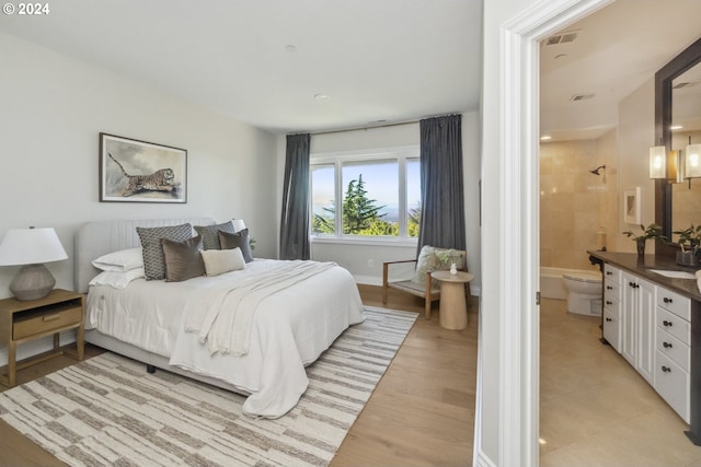 bedroom with light hardwood / wood-style floors, ensuite bath, and sink