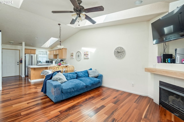 living room featuring vaulted ceiling with skylight, ceiling fan, dark wood-type flooring, and a tile fireplace