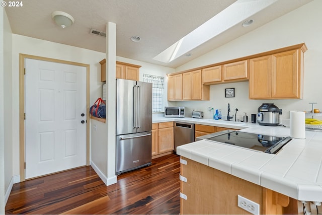 kitchen with tile counters, sink, stainless steel appliances, kitchen peninsula, and vaulted ceiling with skylight