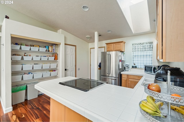 kitchen featuring kitchen peninsula, light brown cabinetry, a textured ceiling, stainless steel appliances, and tile counters