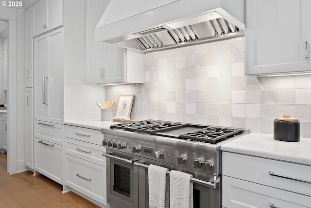 kitchen featuring tasteful backsplash, double oven range, light wood-type flooring, custom range hood, and white cabinetry