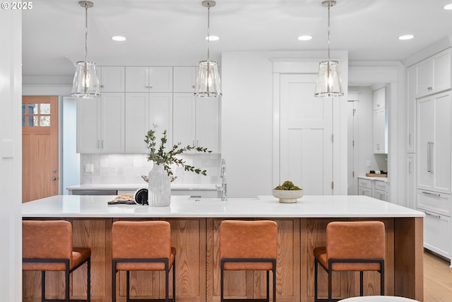 kitchen with a sink, white cabinetry, light countertops, decorative backsplash, and hanging light fixtures