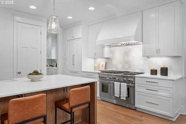 kitchen featuring light wood-style flooring, range with two ovens, a kitchen breakfast bar, and premium range hood