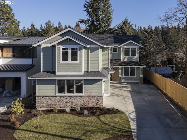 view of front of home featuring stone siding, driveway, roof with shingles, and fence