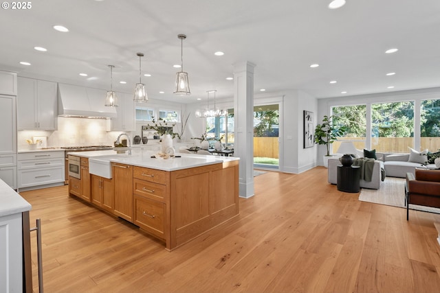 kitchen with premium range hood, light wood-style flooring, decorative columns, light countertops, and open floor plan