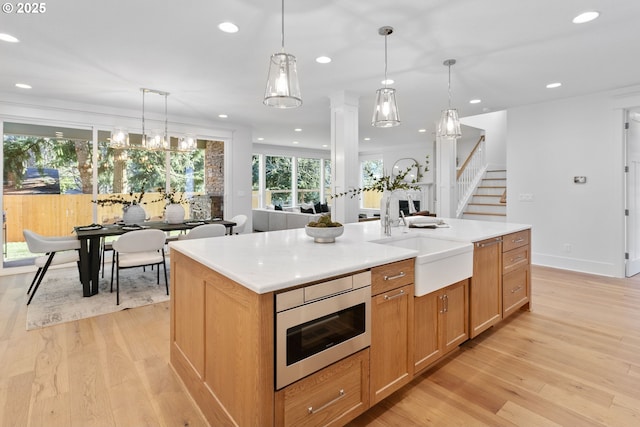 kitchen with light wood-style flooring, an island with sink, a sink, light countertops, and stainless steel microwave