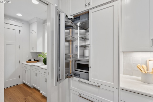 kitchen with light wood-style flooring, recessed lighting, light countertops, white cabinets, and backsplash