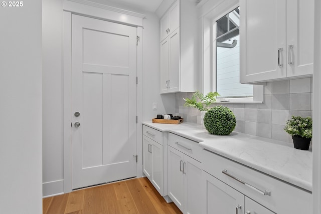 kitchen with light wood finished floors, tasteful backsplash, light stone countertops, and white cabinetry