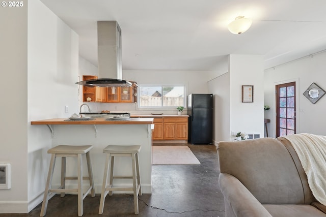 kitchen featuring black refrigerator, plenty of natural light, a kitchen breakfast bar, and island exhaust hood