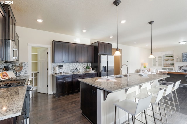 kitchen featuring tasteful backsplash, dark brown cabinetry, open floor plan, appliances with stainless steel finishes, and a sink