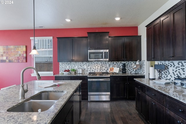 kitchen featuring a sink, decorative backsplash, dark wood-type flooring, appliances with stainless steel finishes, and decorative light fixtures