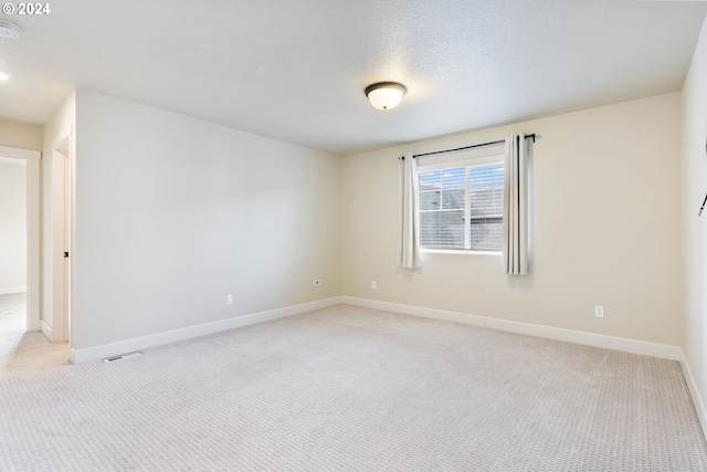 unfurnished room featuring visible vents, light colored carpet, a textured ceiling, and baseboards