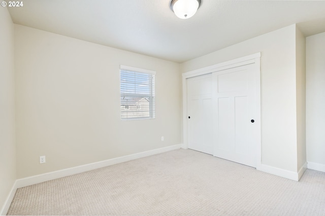 unfurnished bedroom featuring baseboards, a closet, and light carpet