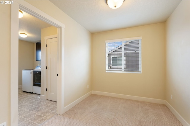 spare room featuring baseboards, light carpet, a textured ceiling, and washing machine and clothes dryer