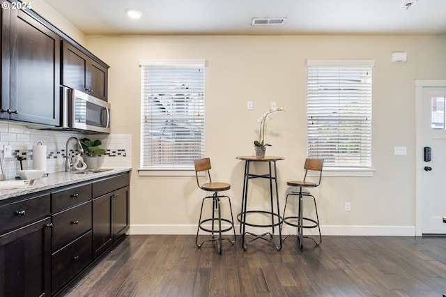 kitchen with visible vents, dark wood-type flooring, light stone counters, stainless steel microwave, and tasteful backsplash