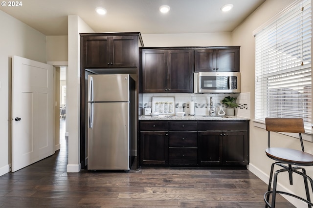 kitchen with stainless steel appliances, backsplash, dark brown cabinets, and dark wood-style flooring