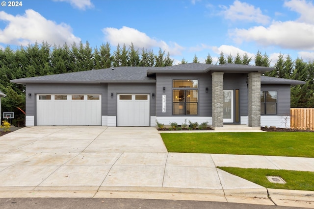 prairie-style house with a front yard, fence, roof with shingles, an attached garage, and concrete driveway