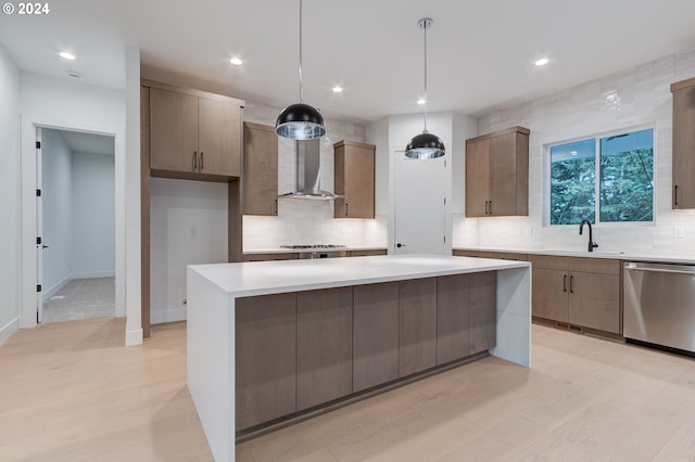 kitchen featuring a sink, light countertops, light wood-style floors, appliances with stainless steel finishes, and wall chimney range hood