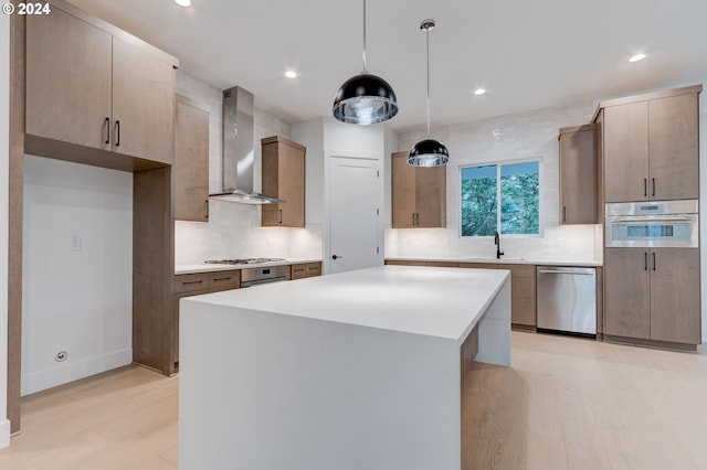 kitchen featuring light wood finished floors, a sink, appliances with stainless steel finishes, wall chimney range hood, and a center island