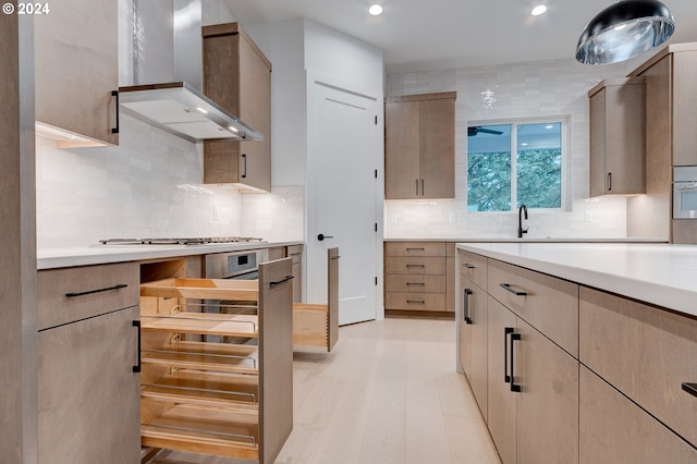 kitchen with light wood-style flooring, stainless steel appliances, light countertops, wall chimney range hood, and backsplash