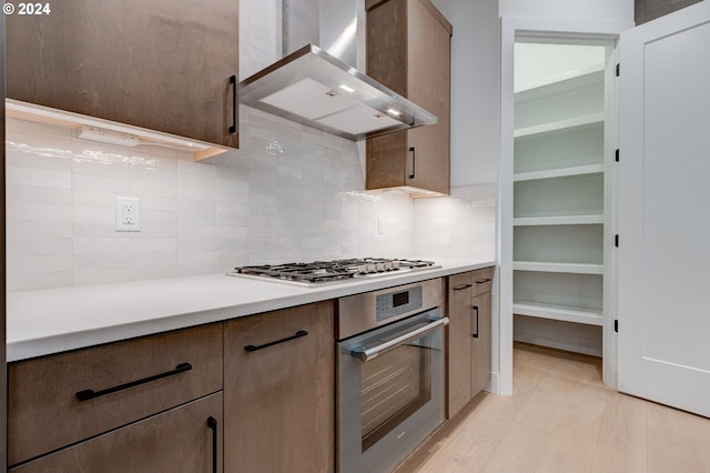 kitchen with stainless steel appliances, wall chimney exhaust hood, decorative backsplash, and light countertops