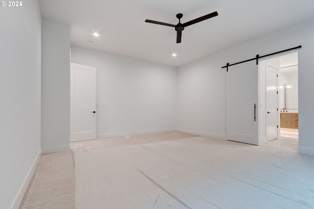 spare room featuring a barn door, light carpet, baseboards, and a ceiling fan