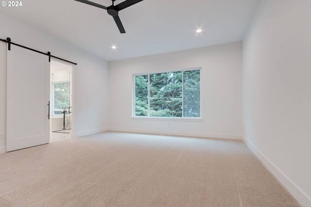 unfurnished room with a barn door, light carpet, plenty of natural light, and ceiling fan