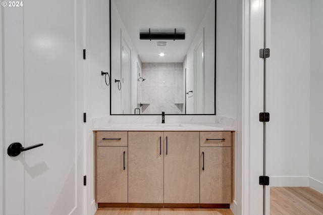 full bathroom featuring a tile shower, vanity, baseboards, and wood finished floors