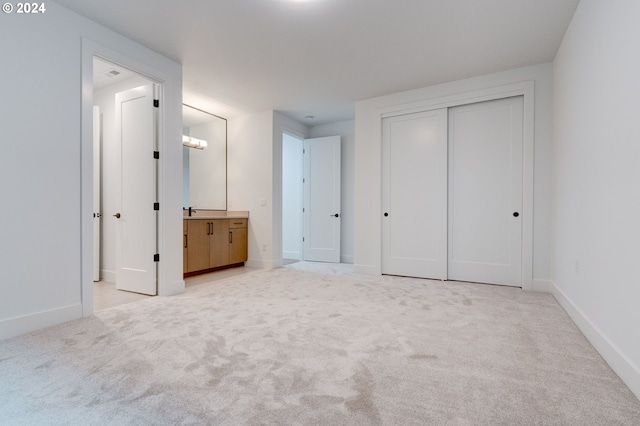 unfurnished bedroom featuring light colored carpet, a closet, ensuite bathroom, and baseboards