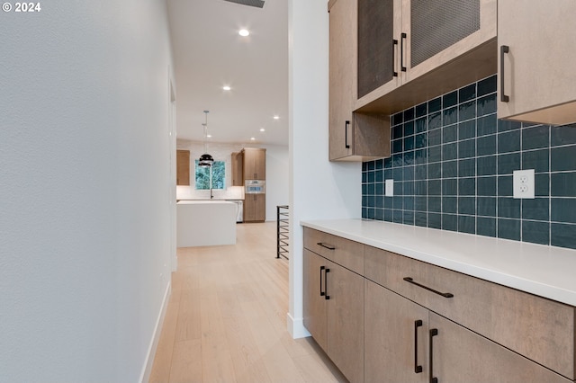 kitchen featuring light wood-style flooring, backsplash, recessed lighting, light countertops, and baseboards