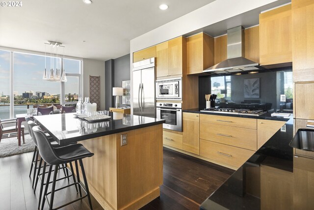 kitchen with wall chimney range hood, hanging light fixtures, dark hardwood / wood-style floors, and built in appliances